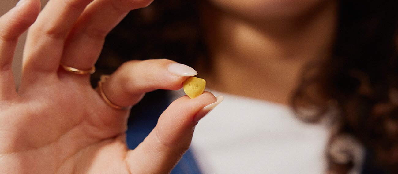 Hände halten eine gelbe Pille in Form eines Schildes