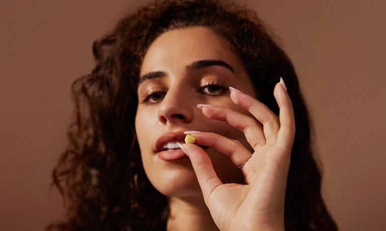 Frau hält Pille in der Hand und blickt in die Kamera